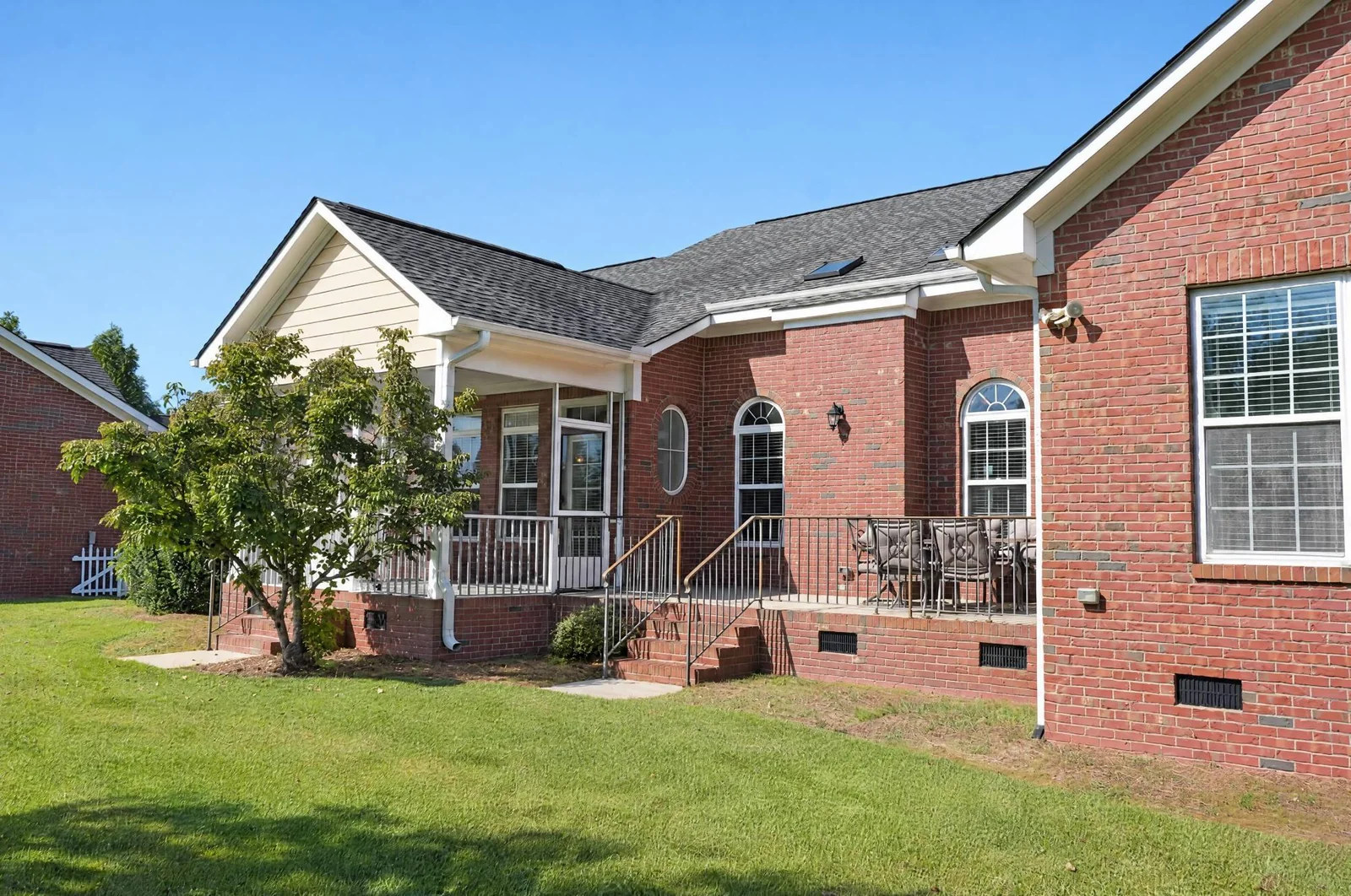 Brick home's rear elevation with a screened porch and open patio